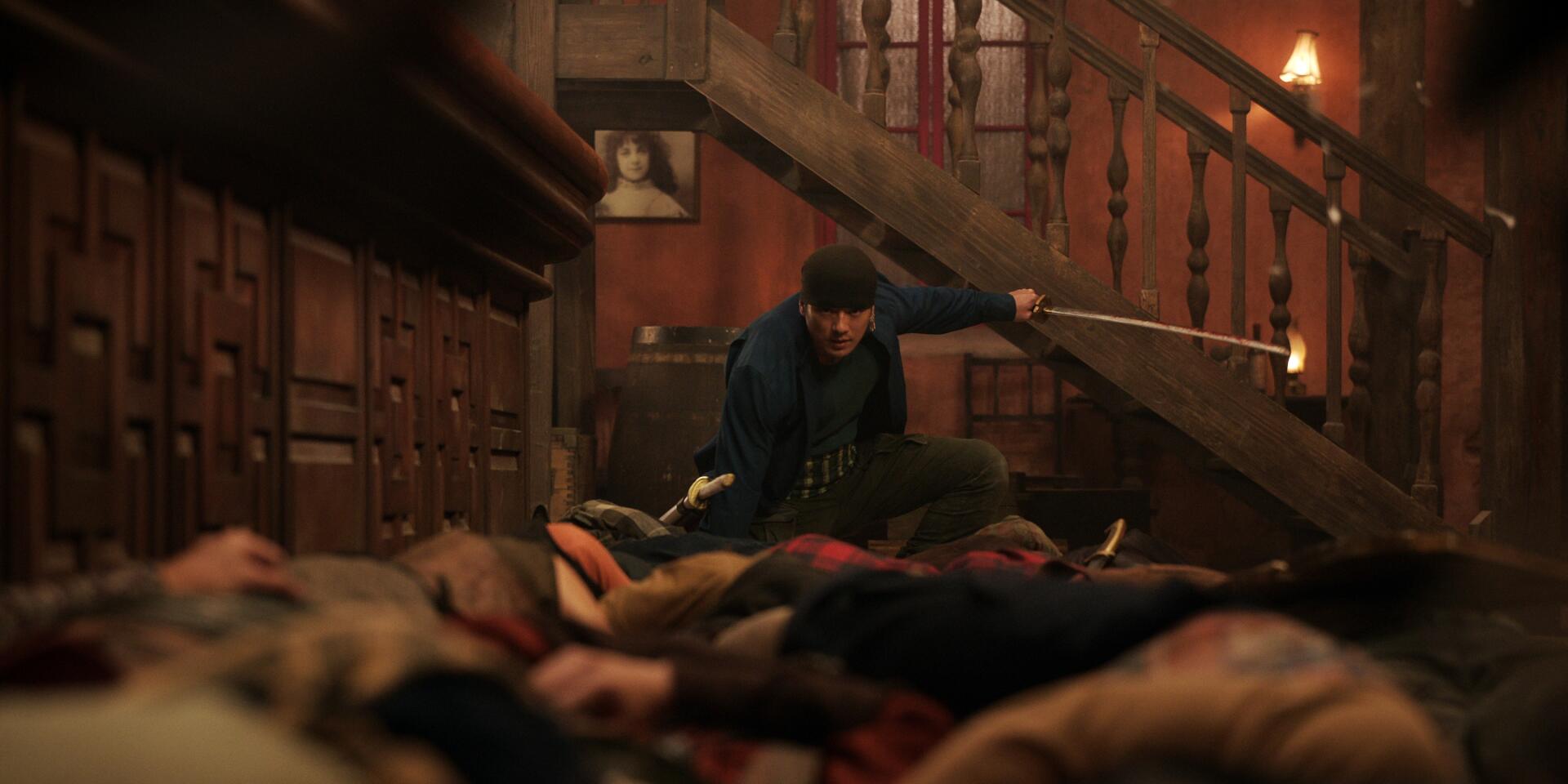 Roronoa Zoro from One Piece (Live Action) kneels amid defeated foes in a dim wooden stairwell, sword drawn — TV show 2K Quad HD PC desktop wallpaper/background.