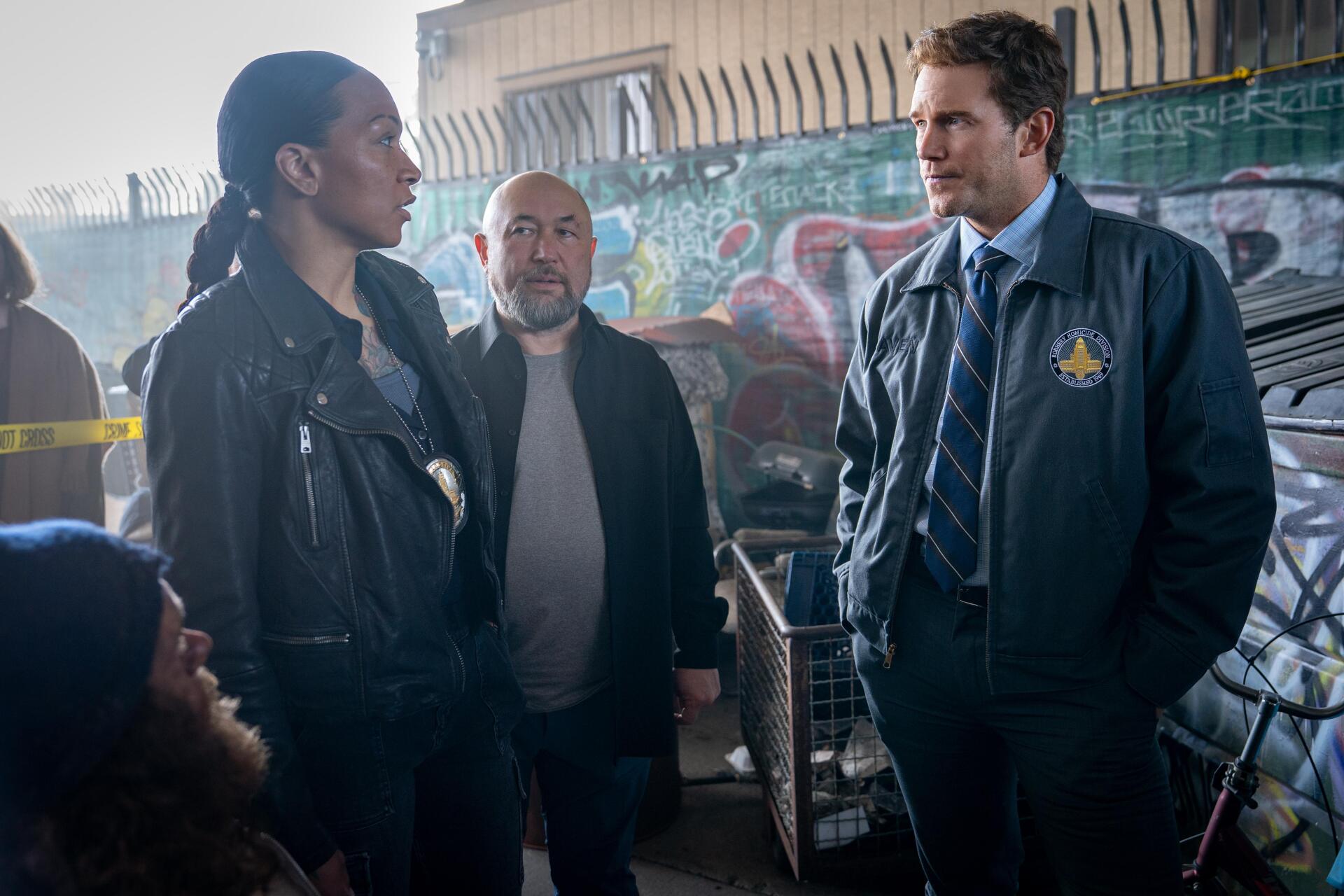 Movie Mercy (2026) still: three investigators in jackets talk in a graffiti-lined alley by police tape — 4K Ultra HD PC desktop wallpaper and background.