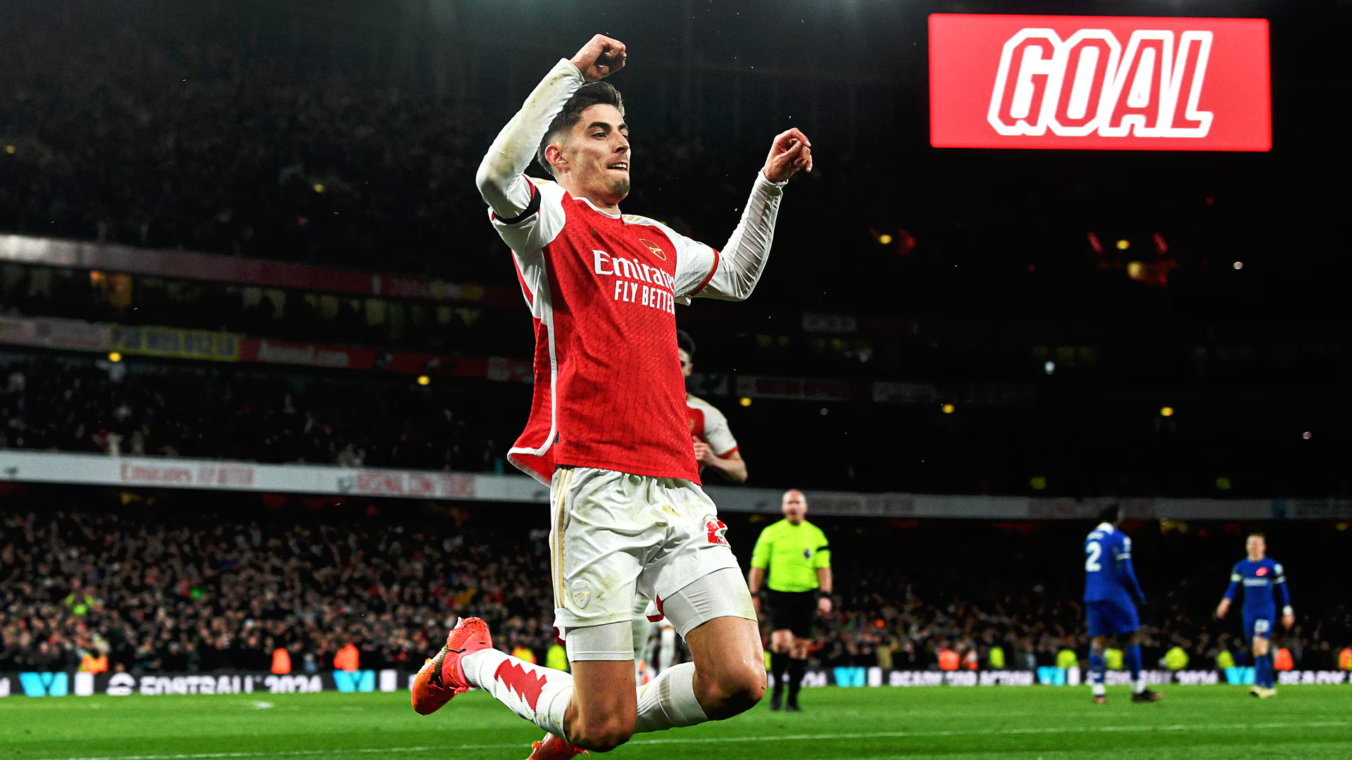 HD PC desktop wallpaper of an Arsenal F.C. player sliding on his knee in celebration on a soccer pitch, stadium crowd and a prominent GOAL sign in the background.