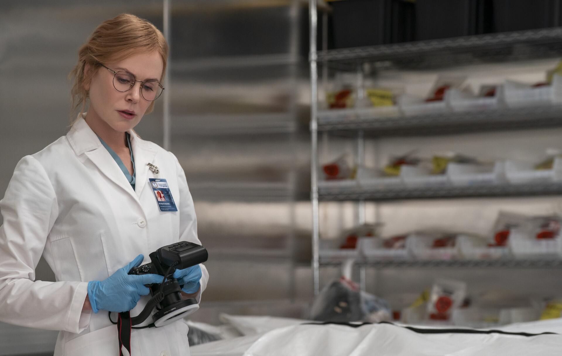 TV show scene: female doctor in white lab coat and blue gloves inspects a covered body in a clinical morgue — 2K Quad HD PC desktop wallpaper.