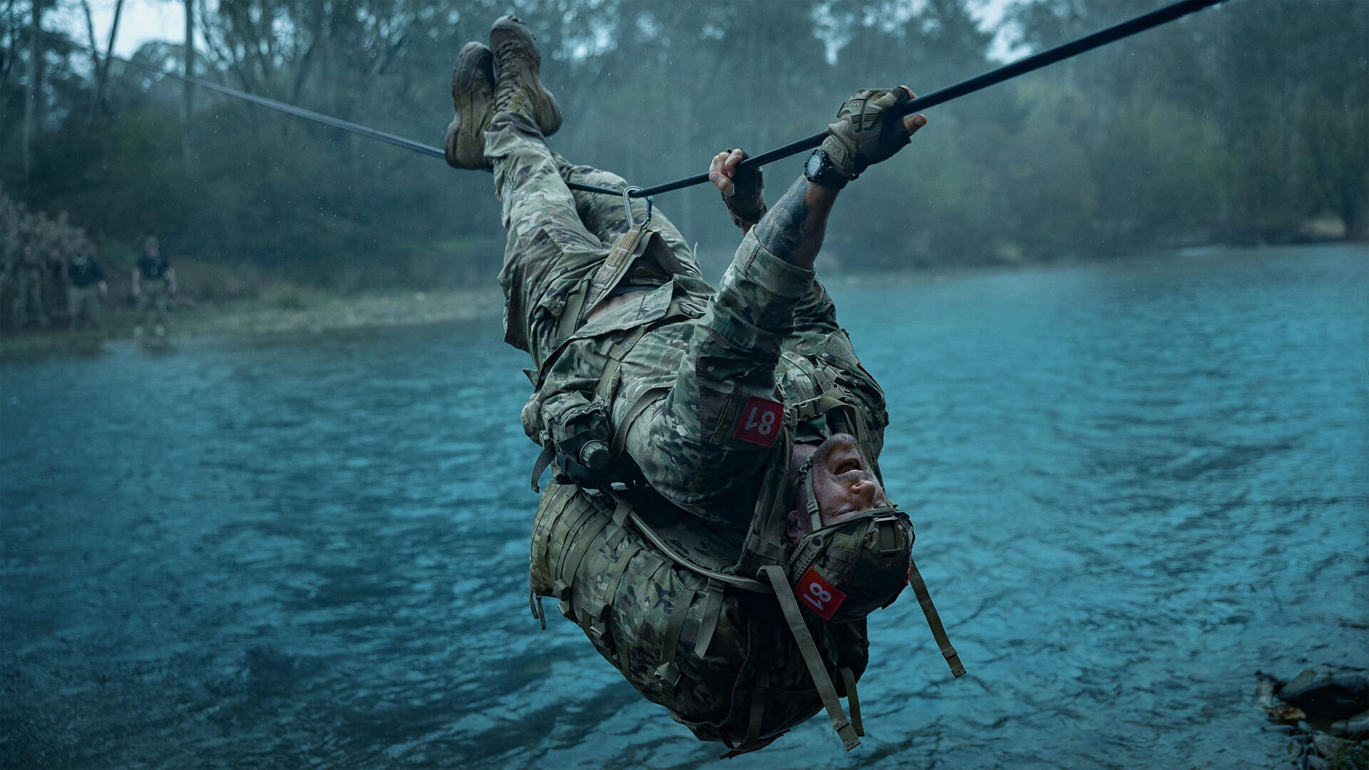 War Machine (2026) 4K Ultra HD PC desktop wallpaper - armored soldier in combat gear dangling from a rope above teal water, rain and mist-shrouded forest in the background.