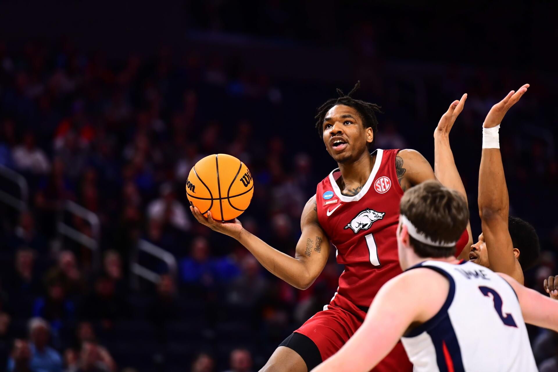 HD desktop wallpaper of an Arkansas Razorbacks player driving for a layup during an NCAA basketball game, a defender reaching up to contest the shot.