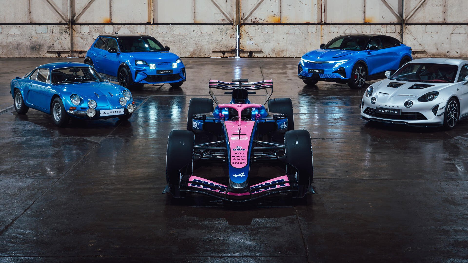 4K Ultra HD desktop wallpaper: Alpine F1 Team pink-and-blue Formula 1 car front and center, flanked by blue and white Alpine road cars in a reflective hangar.