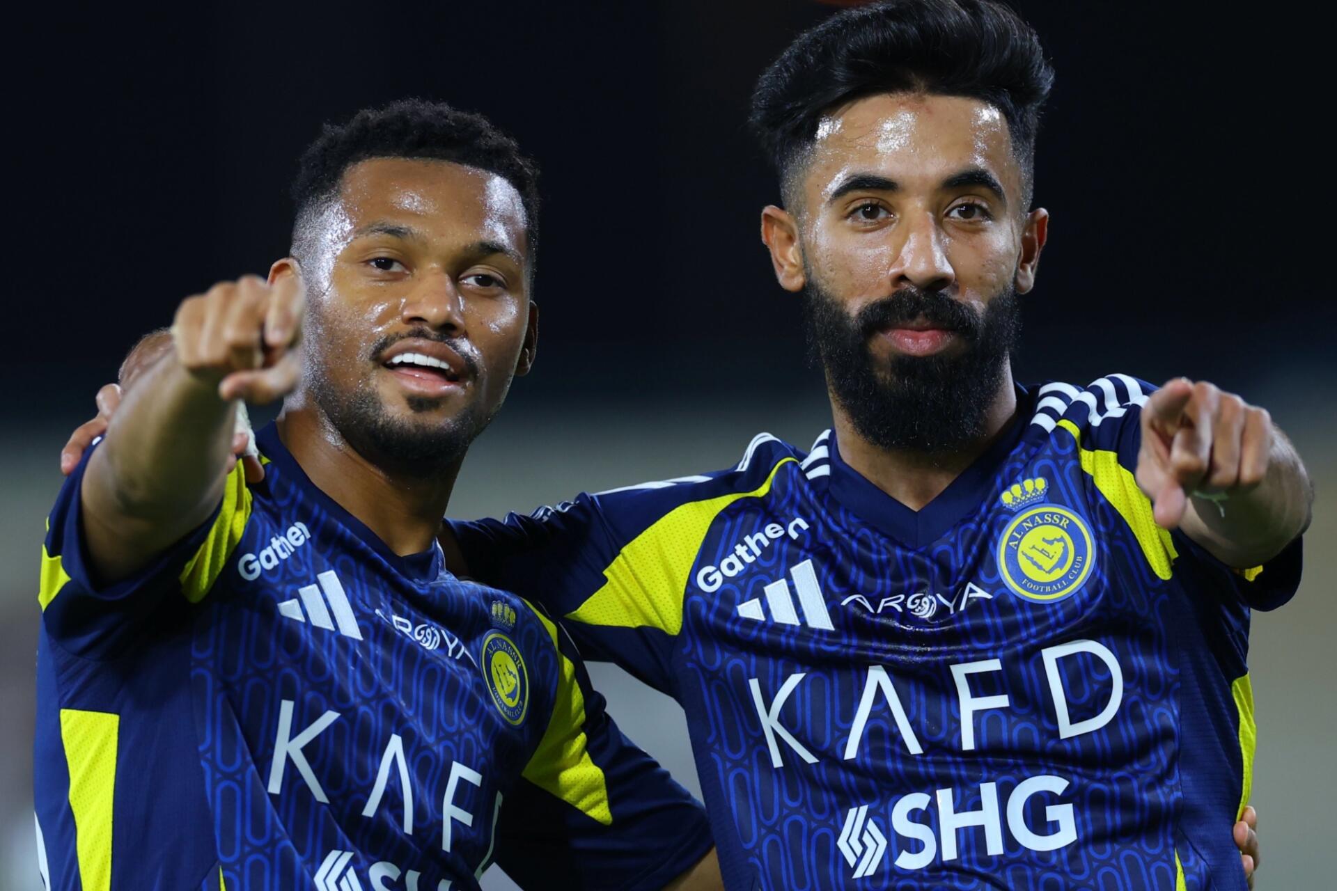 HD PC desktop wallpaper/background: two Al-Nassr FC soccer players in blue-and-yellow kits celebrating on the pitch and pointing toward the camera.