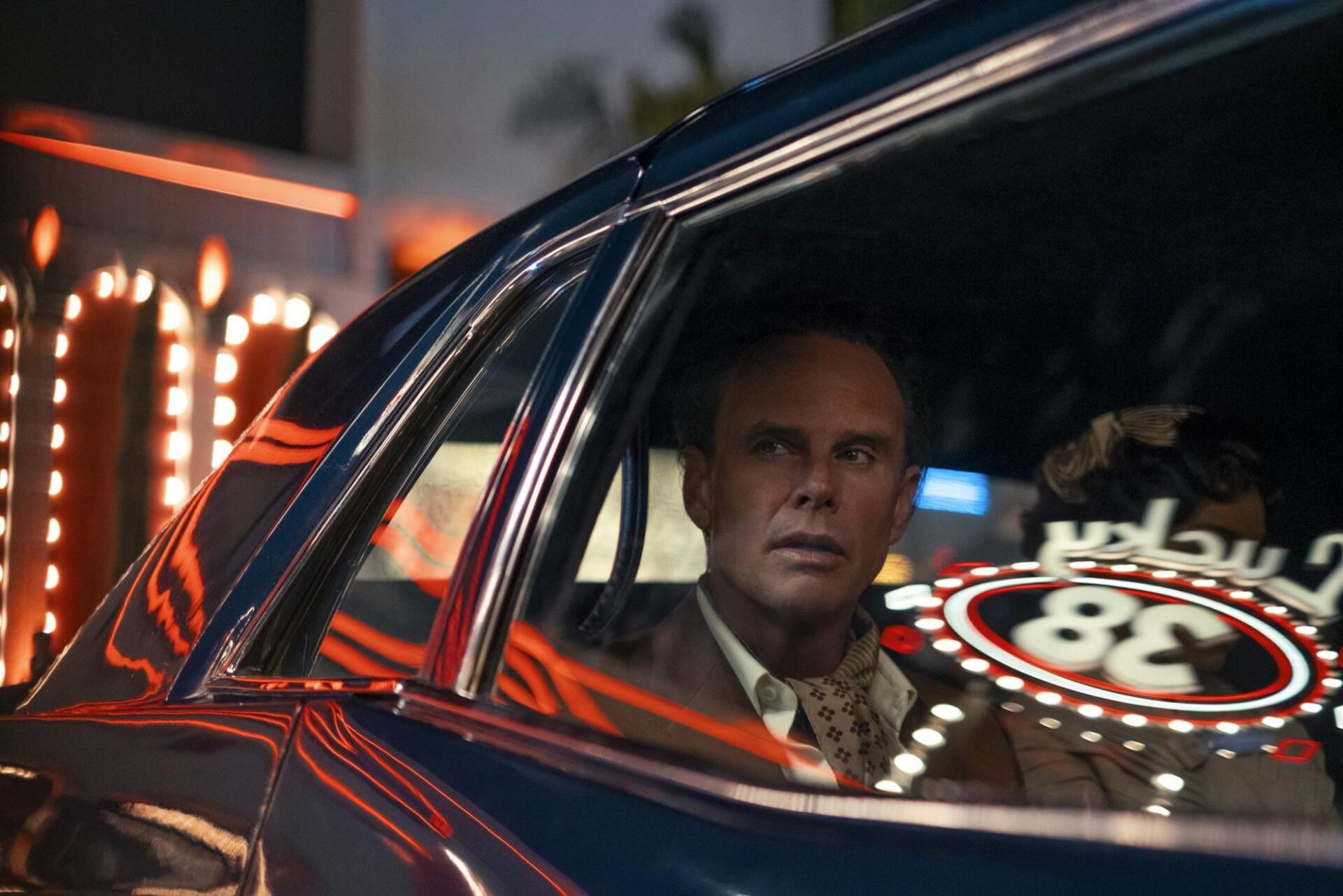 HD PC desktop wallpaper/background from Fallout (TV Show): a tense man in a suit sits inside a retro car, neon casino lights reflected on the window.