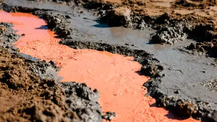 Close-up of wet mud and clay with a vivid orange slurry cutting through dark earth — high-detail 4K Ultra HD PC desktop wallpaper and background.