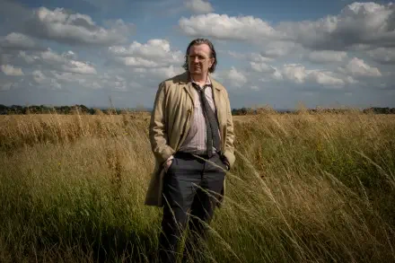 4K Ultra HD desktop wallpaper from TV show Slow Horses: a trench-coated man stands in tall grass under a dramatic, cloud-filled sky.