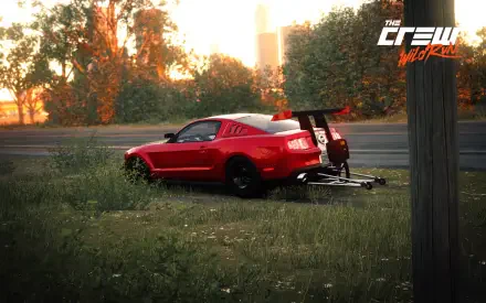Bright daytime HD PC desktop wallpaper: red Ford Mustang drag car with wheelie bar parked on a grassy roadside, The Crew logo in the corner.