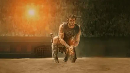 Grizzled gladiator kneels in a sunlit arena, sand and dust swirling — Gladiator II 4K Ultra HD PC Desktop Wallpaper and Background.