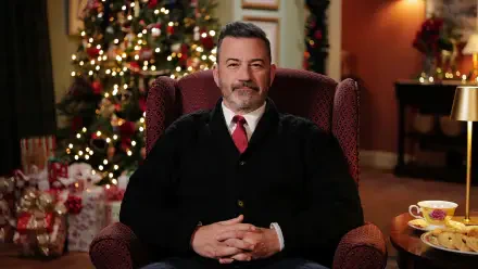 Smiling man in sweater and tie seated in a wingback chair before a decorated Christmas tree, holiday-themed HD desktop wallpaper.