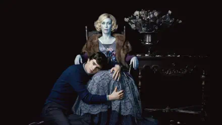 Bates Motel 4K Ultra HD PC desktop wallpaper: moody portrait of a young man clutching an elegant older woman seated in a chair, dark backdrop with a vase of flowers on a side table.