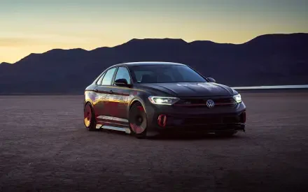 Sleek Volkswagen Jetta parked on desert flat at dusk with mountain silhouette, dark metallic finish and glowing headlights — 2K Quad HD PC desktop wallpaper of a Volkswagen car.