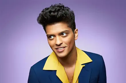 Music-themed HD desktop wallpaper: vibrant portrait of a smiling male pop singer in a blue suit with a yellow open-collar shirt against a soft purple gradient background.