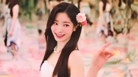 HD PC wallpaper of a smiling K-pop idol singer wearing a pink flower in her hair, radiating summer vibes amid a soft pastel, floral-filled background.