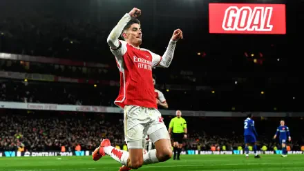 HD PC desktop wallpaper of an Arsenal F.C. player sliding on his knee in celebration on a soccer pitch, stadium crowd and a prominent GOAL sign in the background.