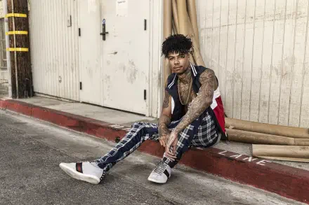 Tattooed rapper in plaid pants and sneakers sits on a curb by a warehouse door, framed as a 5K Ultra HD PC desktop wallpaper/background.