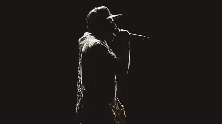 Silhouetted rap singer performing into a microphone against a black background, 2K Quad HD PC desktop wallpaper.
