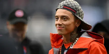 Smiling tattooed man in a patterned cap and orange jacket, 2K Quad HD PC desktop wallpaper.