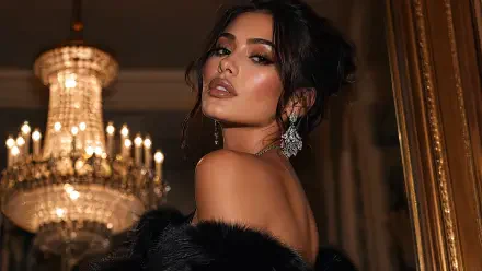 Glam woman in evening gown and fur, jeweled earrings, looking over her shoulder before a crystal chandelier — 4K Ultra HD PC desktop wallpaper and background.