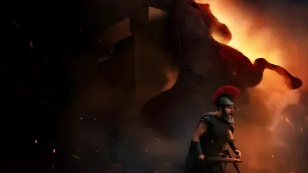 The Odyssey (2026) 4K Ultra HD PC desktop wallpaper and background: armored Greek warrior with red‑crested helmet and spear stands before a towering, fiery shadow of a wooden horse.