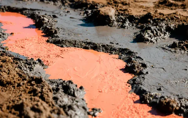 Close-up of wet mud and clay with a vivid orange slurry cutting through dark earth — high-detail 4K Ultra HD PC desktop wallpaper and background.