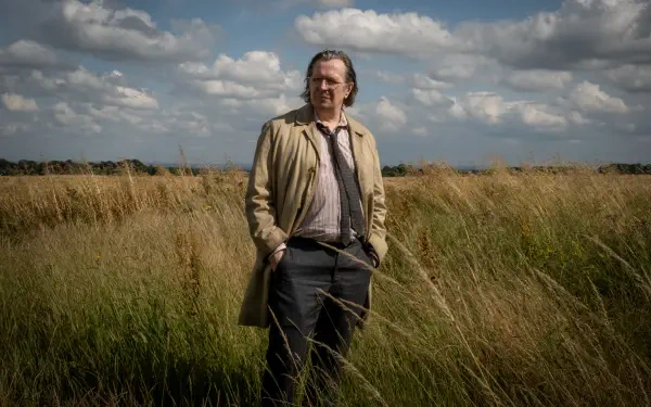 4K Ultra HD desktop wallpaper from TV show Slow Horses: a trench-coated man stands in tall grass under a dramatic, cloud-filled sky.