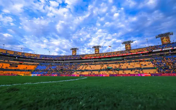 HD PC desktop wallpaper: panoramic view of Cruz Azul stadium and soccer field, lush green pitch beneath a dramatic cloud-filled sky.