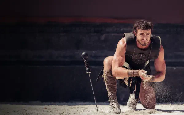 Battle-worn gladiator kneels in sunlit arena sand, gripping helmet and dagger; dramatic cinematic scene — Gladiator II, 4K Ultra HD PC desktop wallpaper and background.