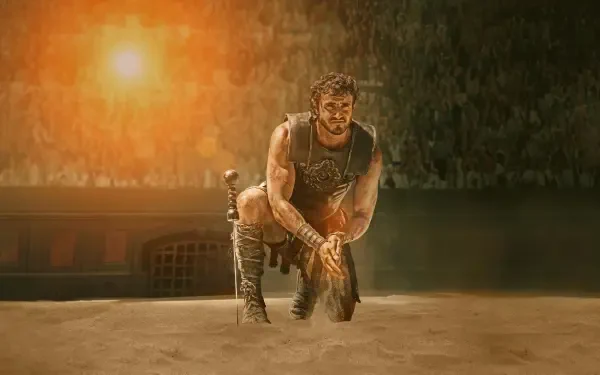 Grizzled gladiator kneels in a sunlit arena, sand and dust swirling — Gladiator II 4K Ultra HD PC Desktop Wallpaper and Background.