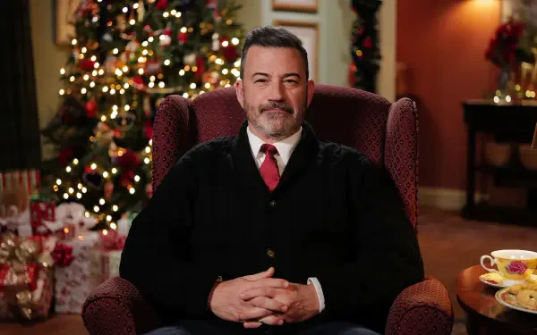 Smiling man in sweater and tie seated in a wingback chair before a decorated Christmas tree, holiday-themed HD desktop wallpaper.