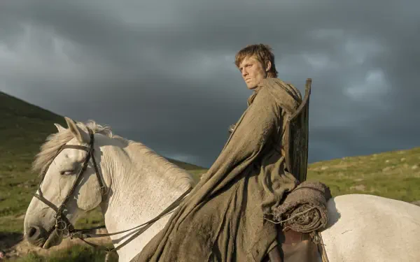 HD PC desktop wallpaper of a cloaked rider on a white horse in windswept hills — a scene from the TV show A Knight of the Seven Kingdoms
