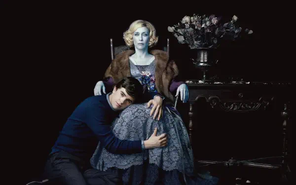 Bates Motel 4K Ultra HD PC desktop wallpaper: moody portrait of a young man clutching an elegant older woman seated in a chair, dark backdrop with a vase of flowers on a side table.