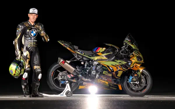 BMW rider stands beside a BMW S1000RR superbike vehicle on a black backdrop — 5K Ultra HD PC desktop wallpaper and background.