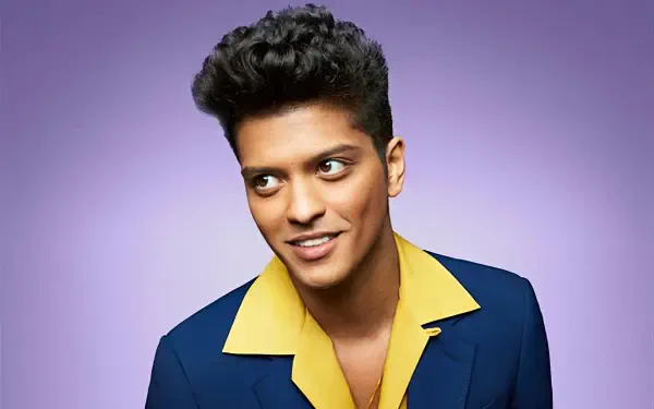 Music-themed HD desktop wallpaper: vibrant portrait of a smiling male pop singer in a blue suit with a yellow open-collar shirt against a soft purple gradient background.