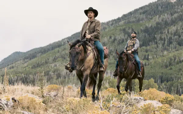 2K Quad HD PC desktop wallpaper: TV show marshals — two cowboys on horseback ride across grassy foothills with forested mountains rising behind them.