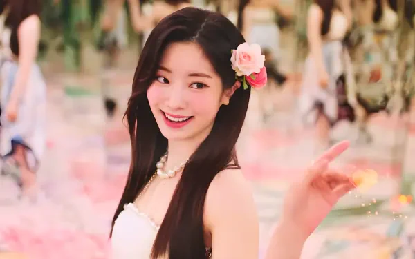 HD PC wallpaper of a smiling K-pop idol singer wearing a pink flower in her hair, radiating summer vibes amid a soft pastel, floral-filled background.