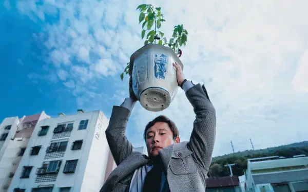 No Other Choice — 4K Ultra HD PC desktop wallpaper showing a man hoisting a potted plant overhead against a cloudy blue sky above city rooftops.