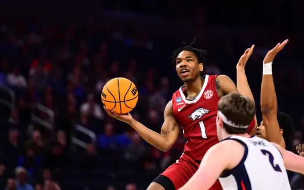HD desktop wallpaper of an Arkansas Razorbacks player driving for a layup during an NCAA basketball game, a defender reaching up to contest the shot.