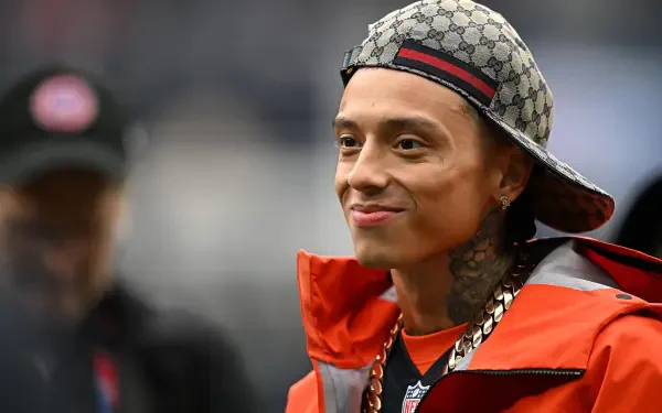 Smiling tattooed man in a patterned cap and orange jacket, 2K Quad HD PC desktop wallpaper.