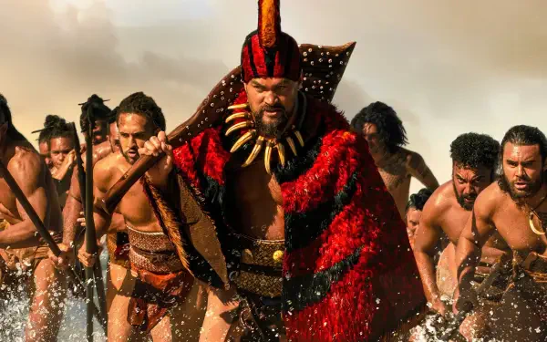 Chief of War leads a charging warband through surf, clad in a red feathered cloak and tooth necklace, warriors with spears behind — 4K Ultra HD PC desktop wallpaper/background.