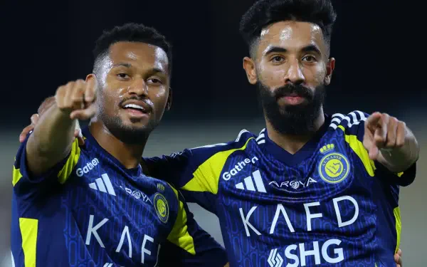 HD PC desktop wallpaper/background: two Al-Nassr FC soccer players in blue-and-yellow kits celebrating on the pitch and pointing toward the camera.