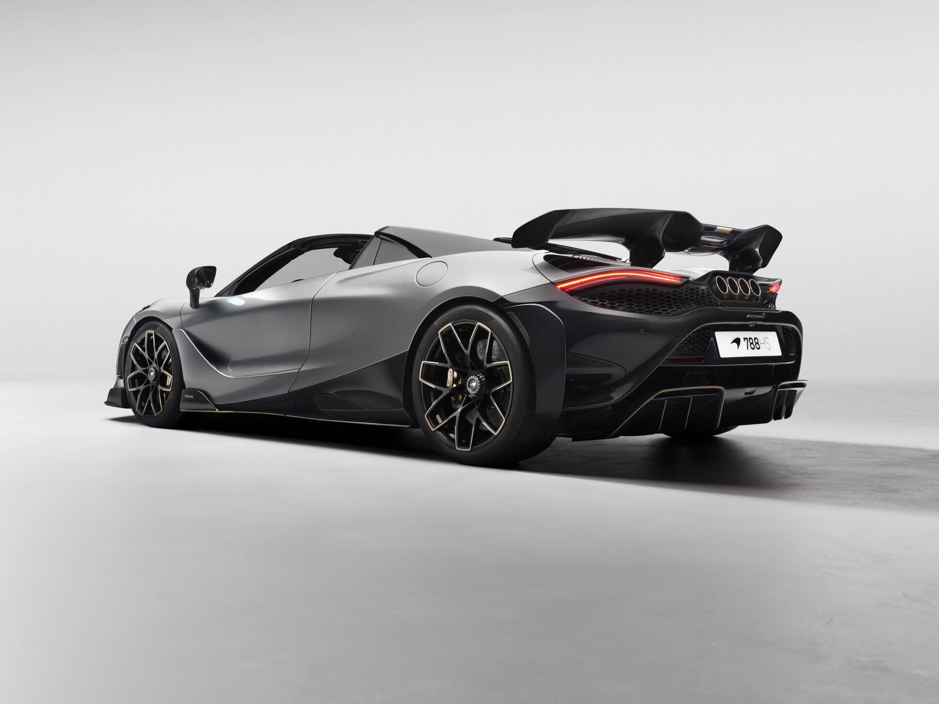 Silver McLaren 788HS roadster, rear three-quarter view with raised wing, studio-lit on a neutral backdrop — 8K Ultra HD PC desktop wallpaper vehicle image.