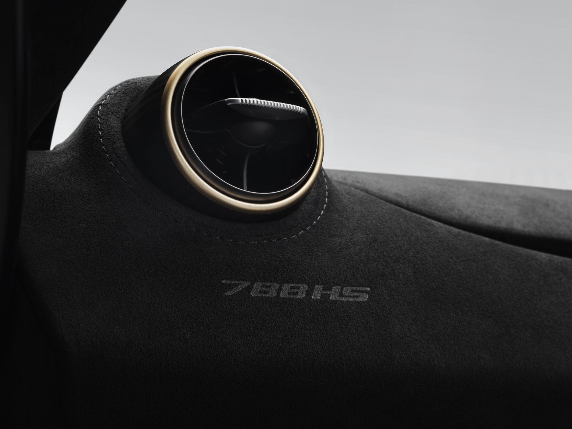Close-up of a McLaren 788HS dashboard with a round gold-trimmed air vent and embossed 788HS on Alcantara — 8K Ultra HD PC desktop wallpaper/background of a McLaren vehicle.