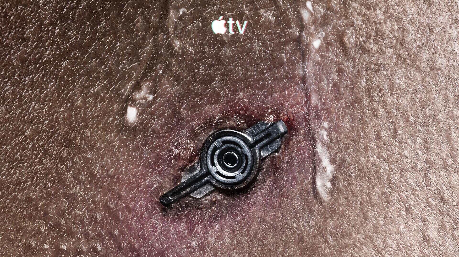 Close-up textured surface with a central dark metallic mechanical emblem and a small Apple TV logo above — 4K Ultra HD PC desktop wallpaper and background.