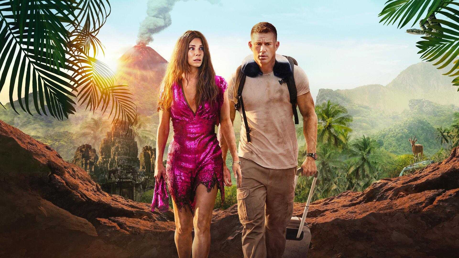 The Lost City (2022) 4K Ultra HD PC desktop wallpaper: woman in a fuchsia dress and man with a backpack and shovel trekking a jungle path toward an erupting volcano, palm fronds framing them.