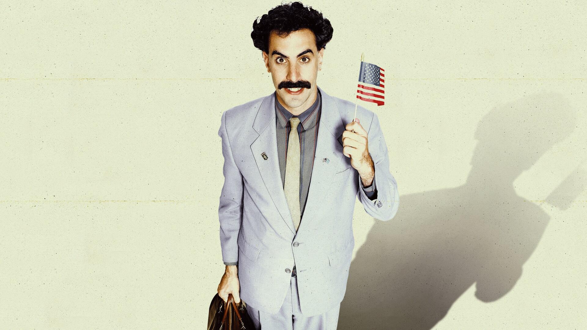 Borat Subsequent Moviefilm 4K Ultra HD PC desktop wallpaper: the Borat character in a light gray suit holding a small U.S. flag and briefcase, casting a long shadow on a pale background.