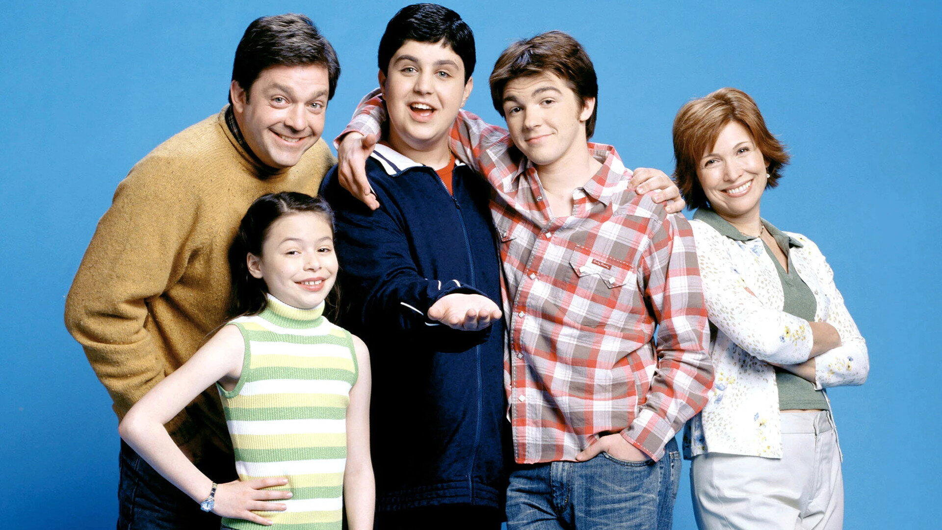 HD PC desktop wallpaper of a smiling sitcom cast — two teen boys, a girl and two adults posed against a blue background.