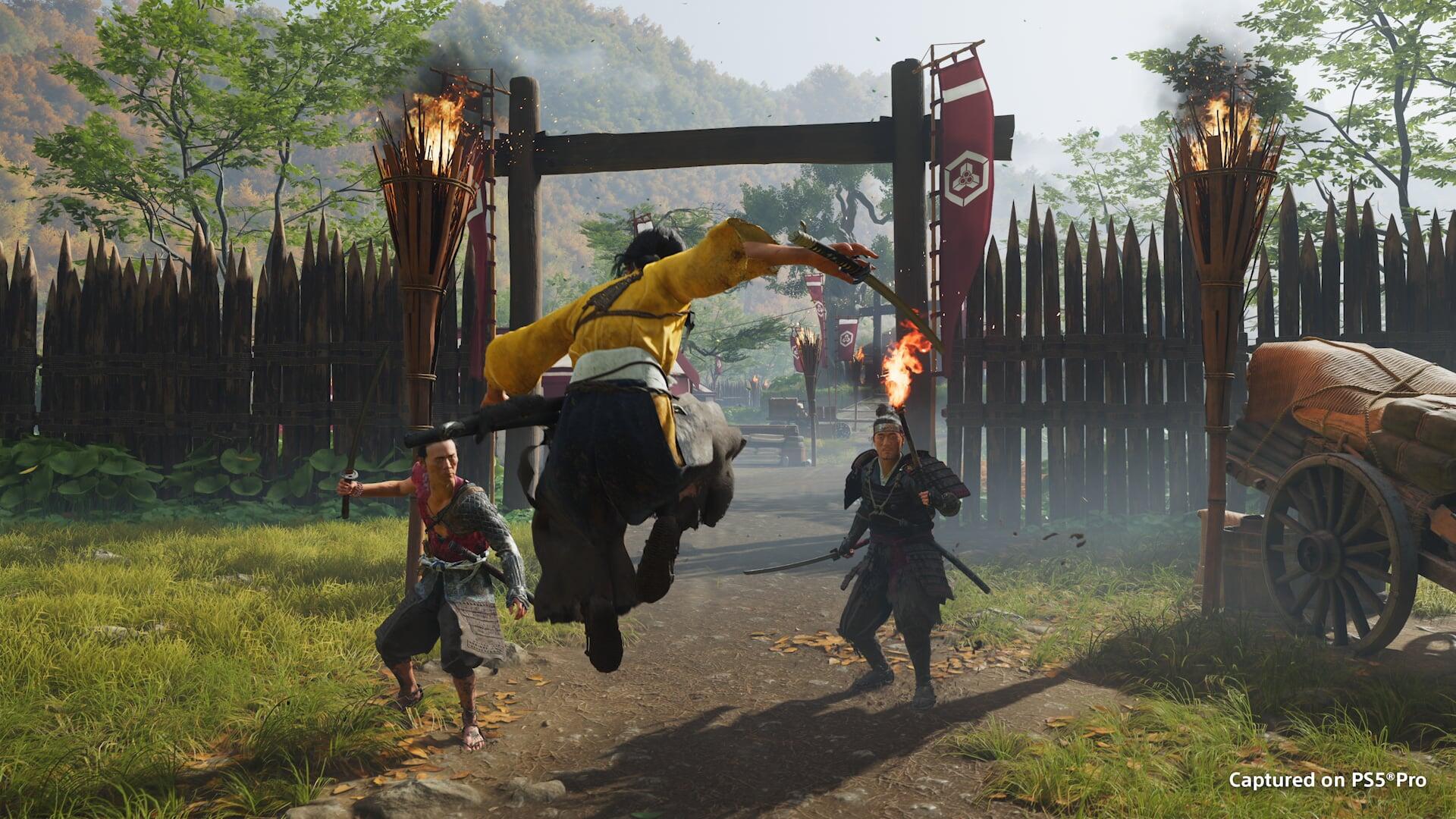 HD PC desktop wallpaper/background from Ghost of Yōtei: a samurai in yellow leaps through a gate, sword raised amid torches and a wooden palisade during a fierce battle.
