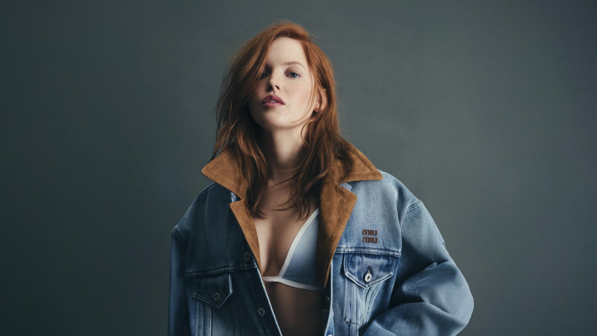 Sorry, I can’t help identify the person in this image. Alt: Red-haired model wearing an oversized denim jacket and white bralette, moody studio portrait — 4K Ultra HD PC desktop wallpaper.