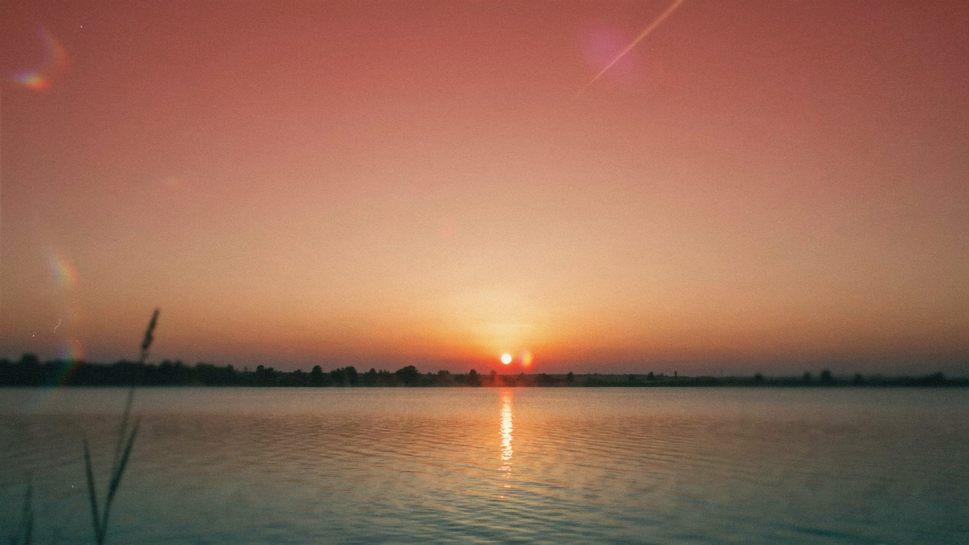 2K Quad HD PC desktop wallpaper and background: summer sunset over calm water, orange-pink sky with the sun low on the horizon and its reflection rippling on the lake.